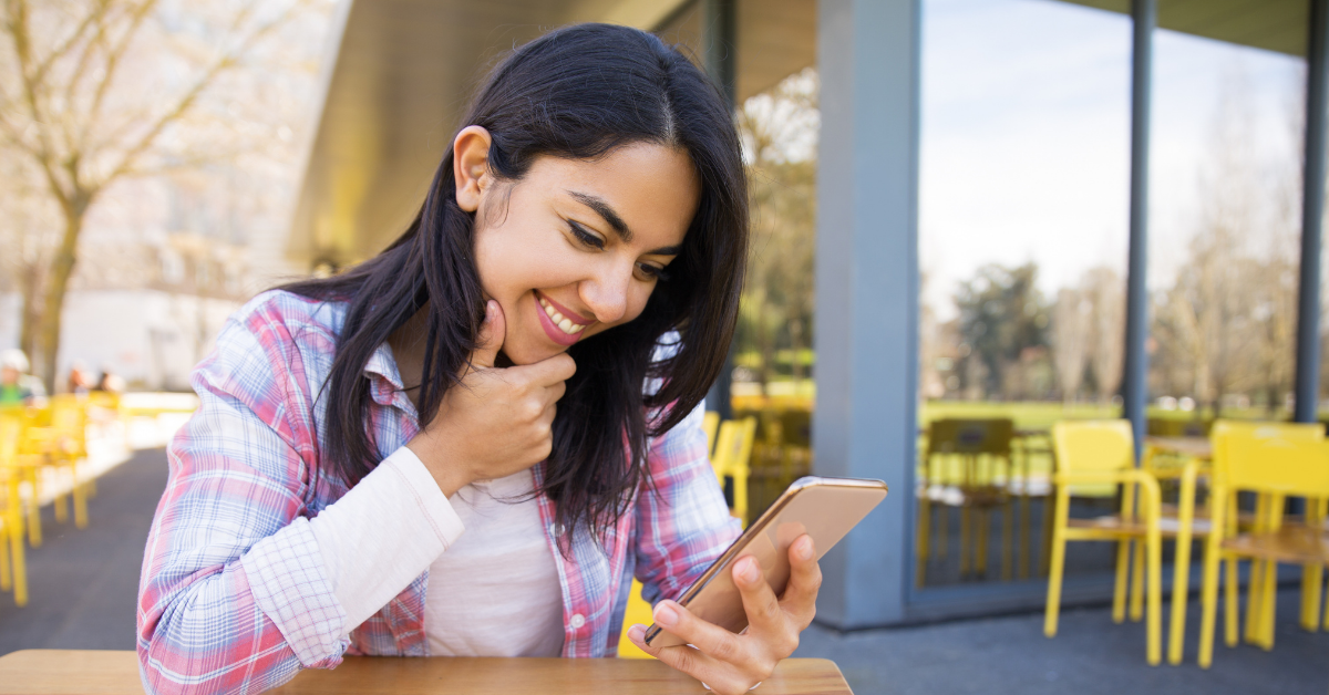 smiling young woman looking at her phone while sitting outside