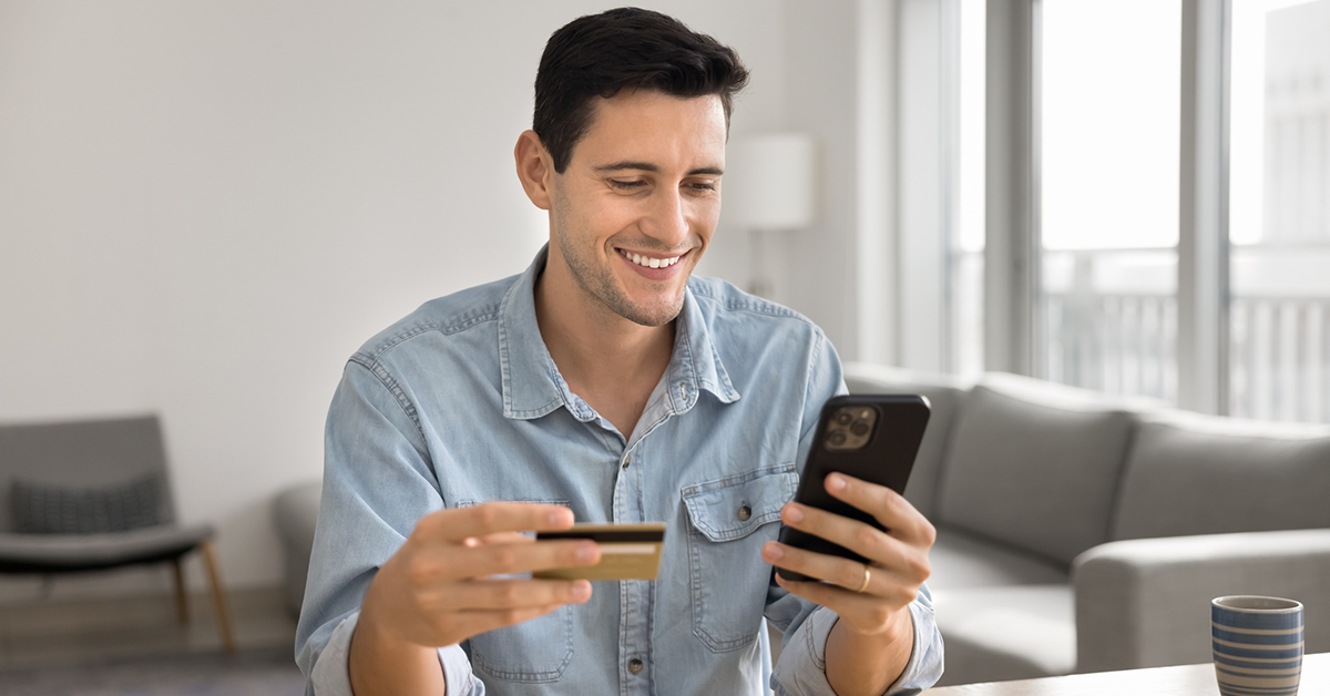 smiling young man with a credit card looking at a phone