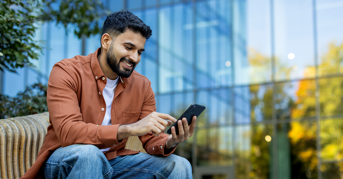 young man sitting outside of a building while looking at his phone