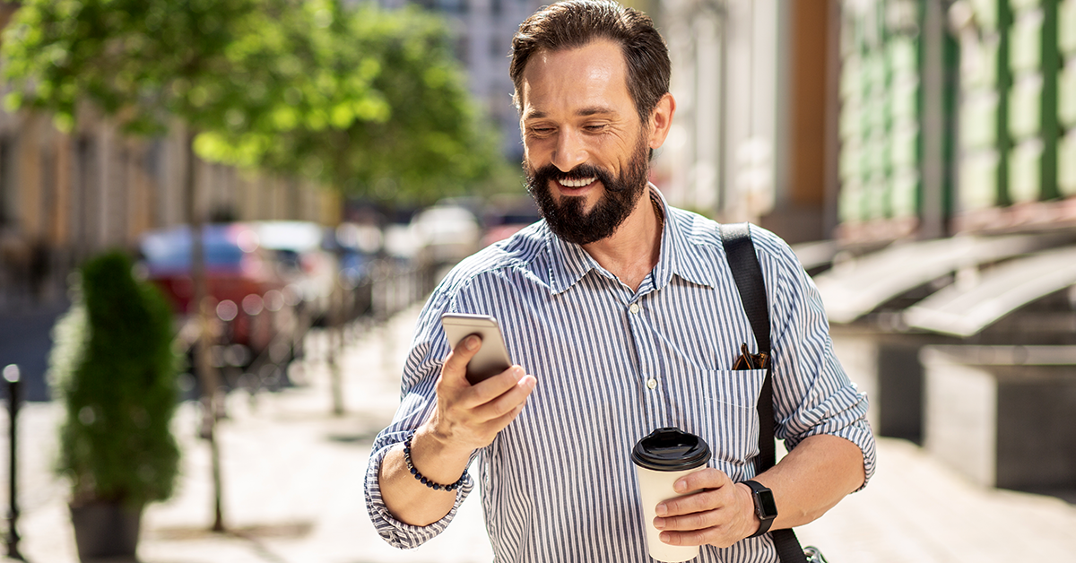 smiling man walking outside while looking at his phone