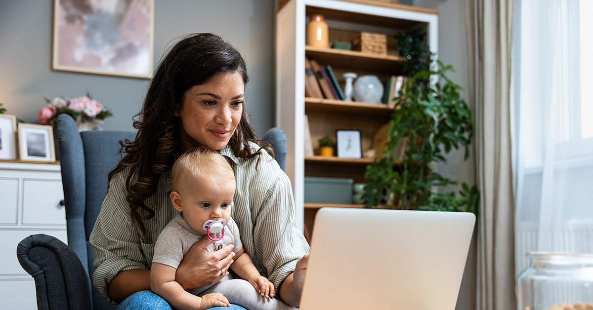 mom looking at a laptop while holding a baby