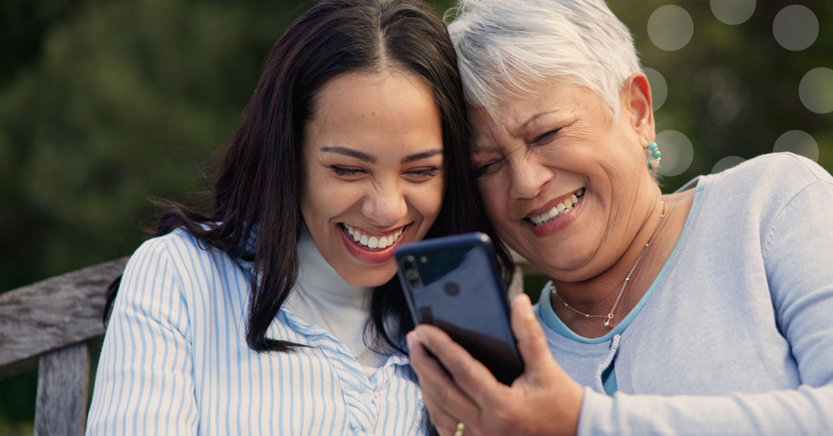 smiling adult daughter and senior mother looking at a cell phone