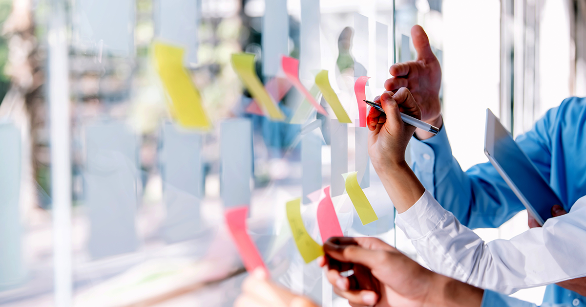 people putting sticky notes on a clear workboard