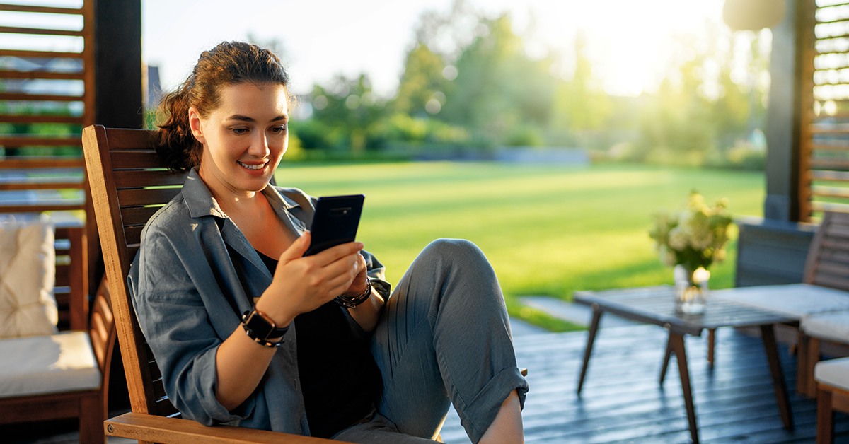 smiling woman sitting on an outside patio looking at her phone