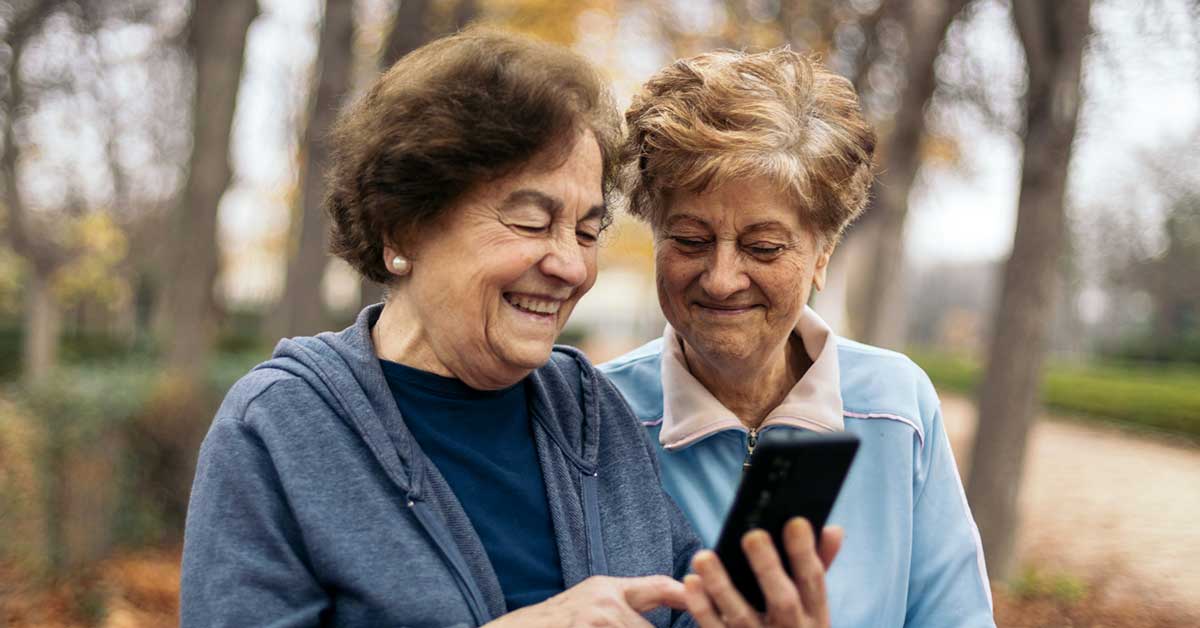 two smiling seniors sitting outside looking at phone