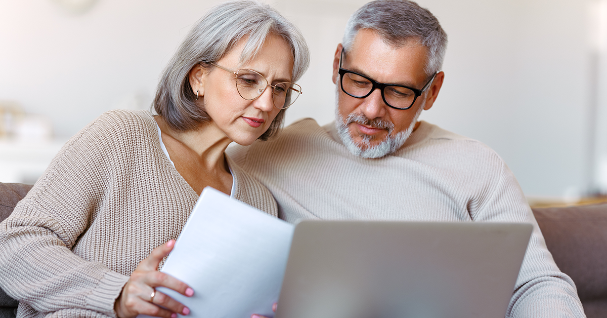 seniors sitting on a couch reviewing a document and looking at a computer