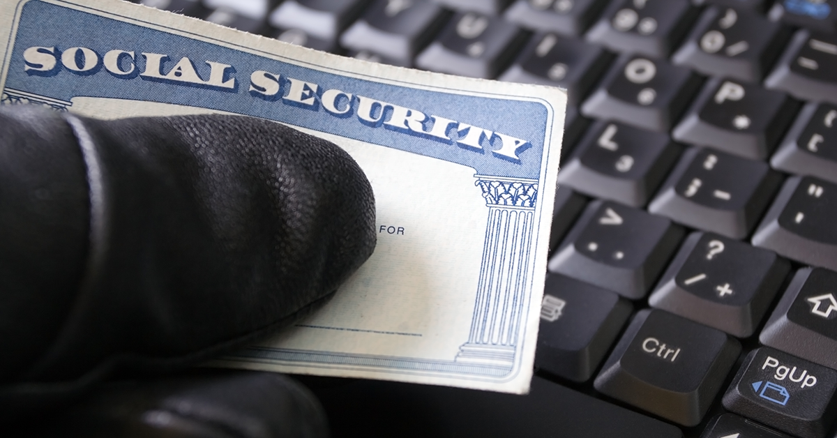 gloved hand holding a social security card over a keyboard