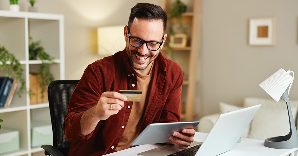 smiling man looking at a credit card working at his desk