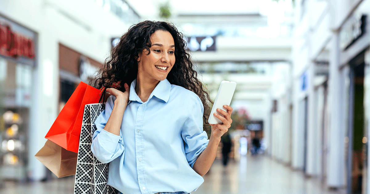 a smiling young woman shopping with store bags in one hand and the phone in another