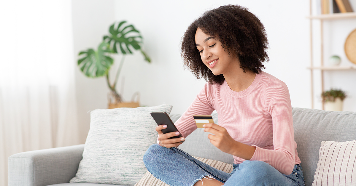 young woman sitting on a couch using her phone and credit card