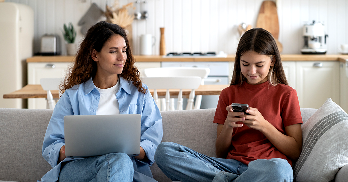 mother and daughter sitting on couch with laptop and phone
